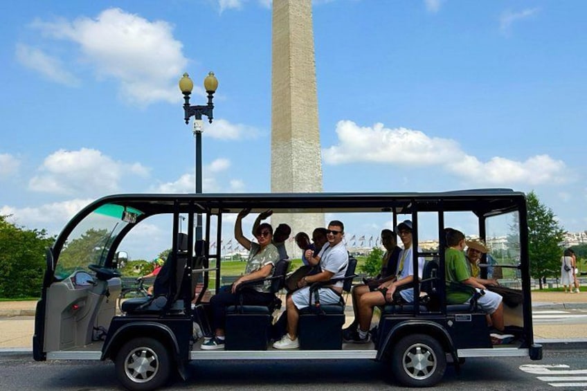 En grupp människor i en sightseeingbuss nära ett högt monument. 4