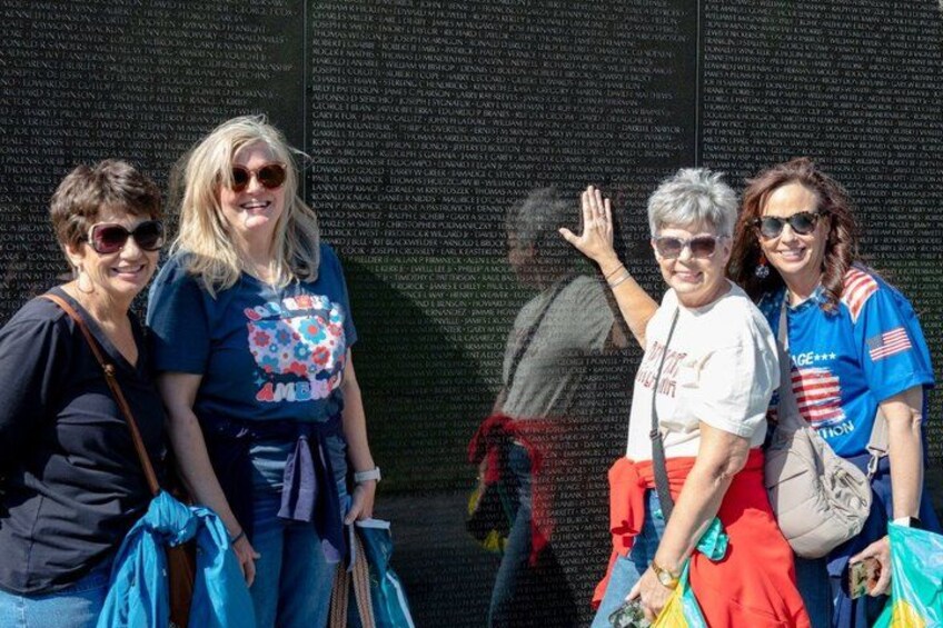 A memorial wall with engraved names, people posing in front of it, and a clear sky. 3