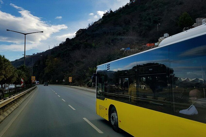 En gul bus på en vej med flere baner, med et bjerg i baggrunden. 5