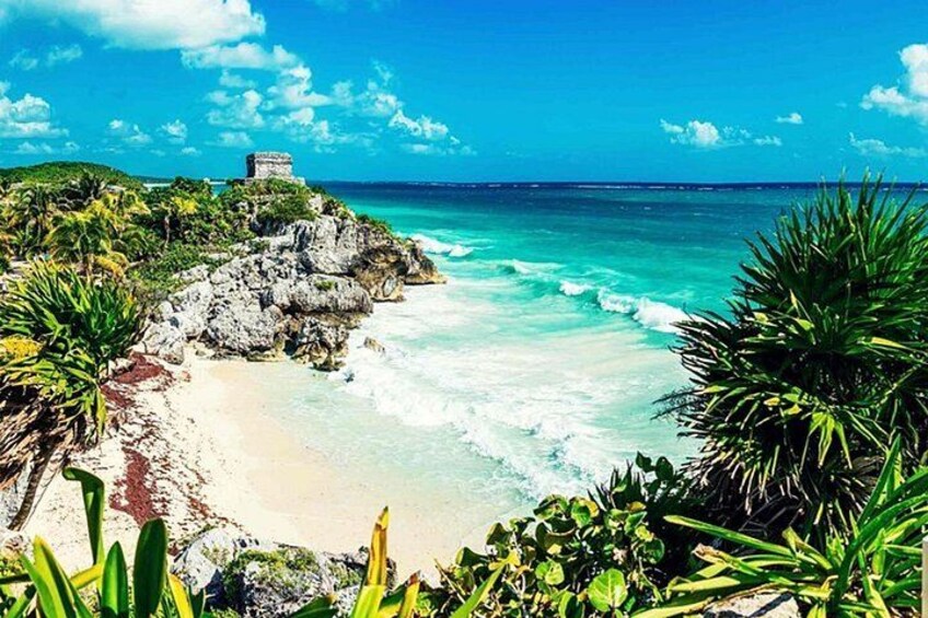 A coastal landscape with a beach, rocky outcrops, and lush vegetation. 1
