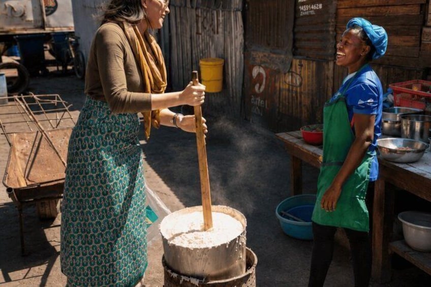 Two women cooking outdoors, one stirring a large pot and the other standing by a table with cooking utensils. 4