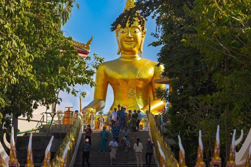 Eine große goldene Buddha-Statue, umgeben von Bäumen und Menschen. 2