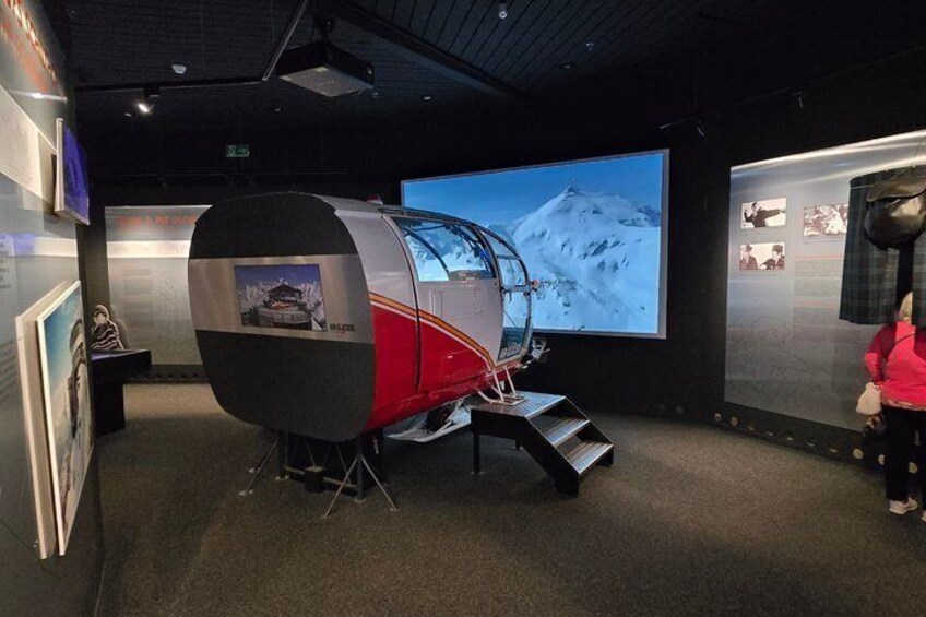 A museum exhibit with a large display case, a projection screen, and informational panels. 4