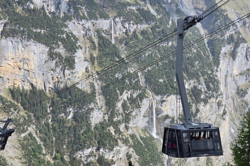 A cable car suspended over a mountainous landscape with a waterfall in the background. 2
