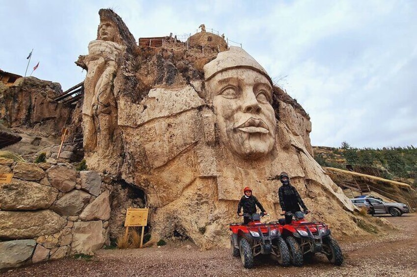 A large rock formation with a carved face, a wooden sign, and two ATVs. 1