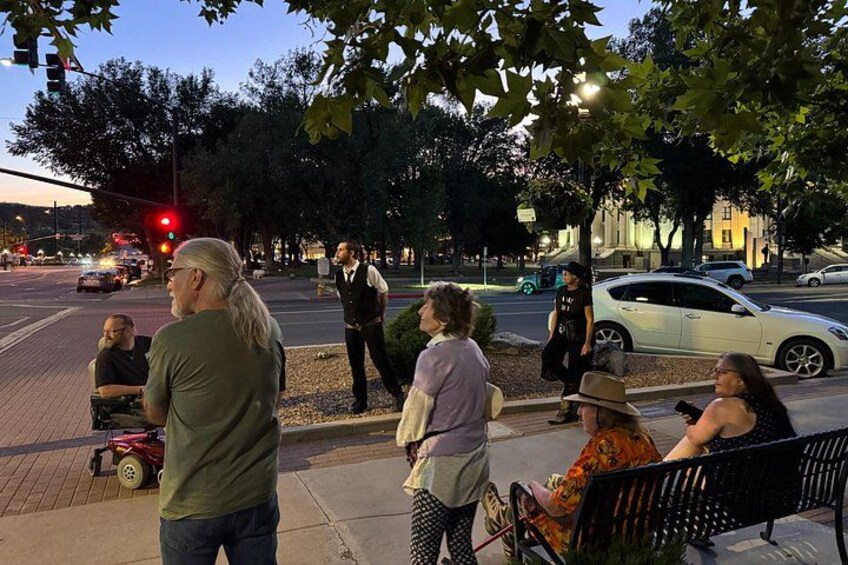 A group of people on a sidewalk, a street with cars, and a traffic light. 2