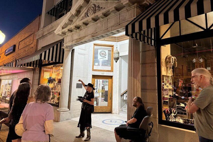 A street scene with a person gesturing towards a shop entrance, a building with columns, and a storefront with mannequins. 3