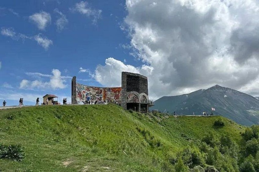 A grassy hill with a large, weathered structure featuring circular arches and a steep incline. 5