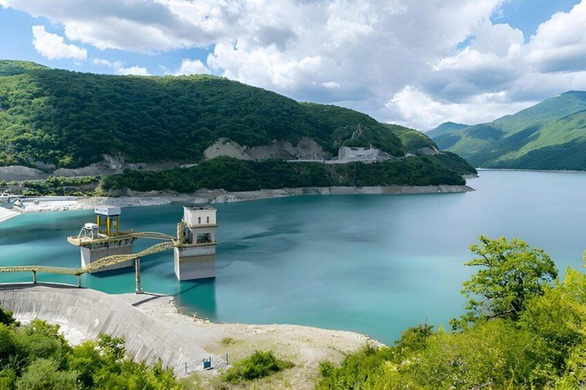 A calm lake surrounded by green hills, a small island with a structure, and a dock with a boat. 2