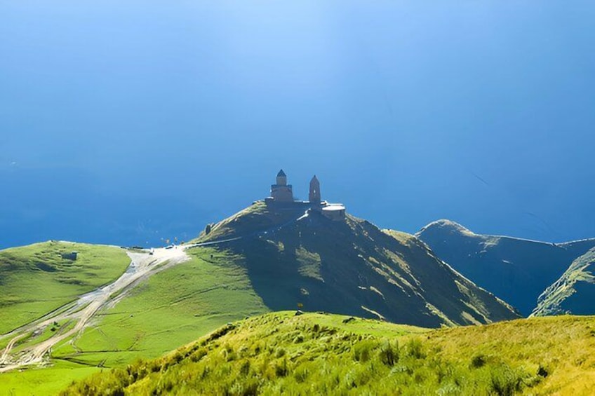 A grassy hill with a small building on top, surrounded by rolling hills and a clear sky. 2