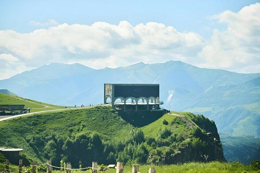 Ein Gebäude auf einem Hügel, im Hintergrund Berge. 2