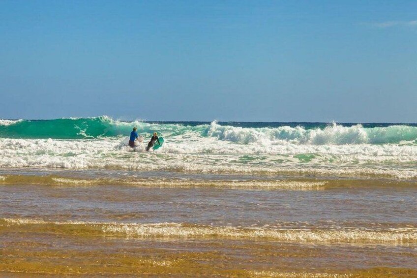 A beach with waves and two people in the water. 3