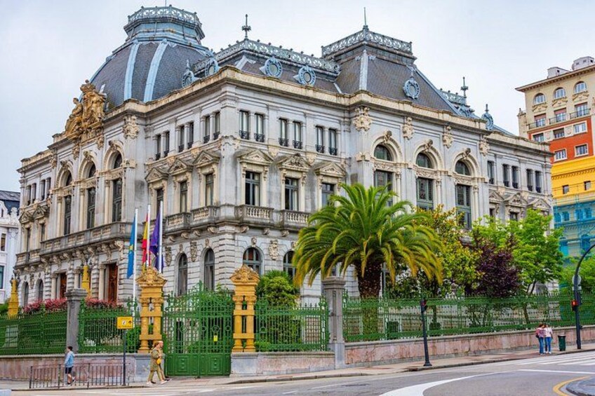 A historic building with ornate architecture, a green fence, and palm trees. 3