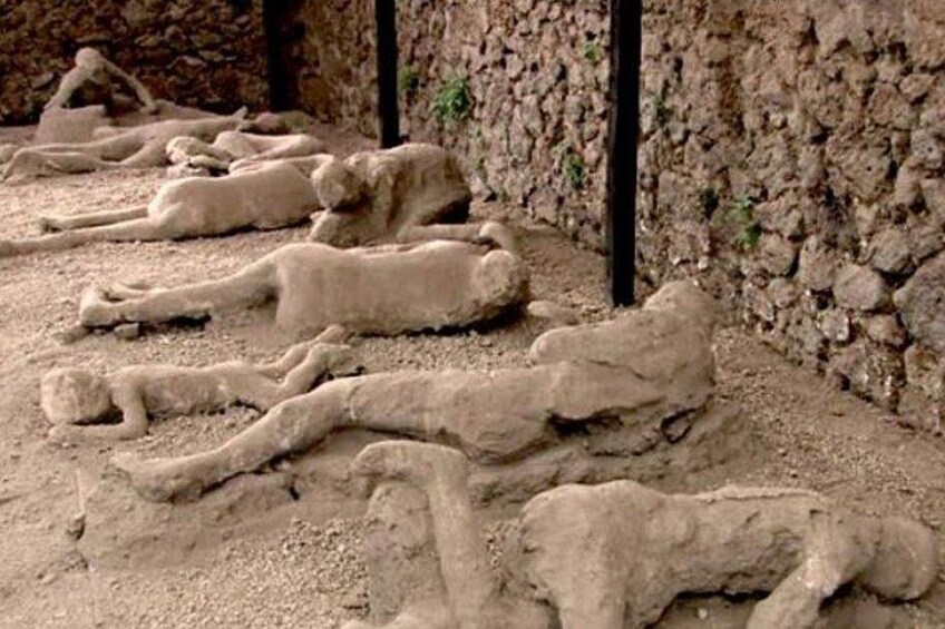 Una serie de esculturas de piedra que representan figuras reclinadas en una zona arenosa con muros de piedra. 3
