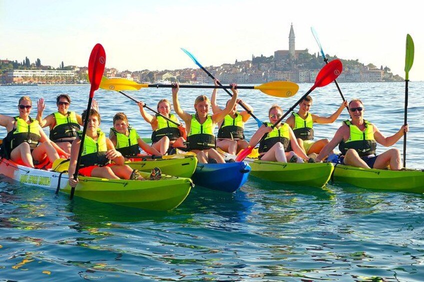 A group of people in green kayaks on a body of water with a cityscape in the background. 1