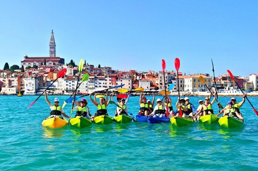 A group of people in colorful kayaks rowing on a calm body of water with a cityscape in the background. 5