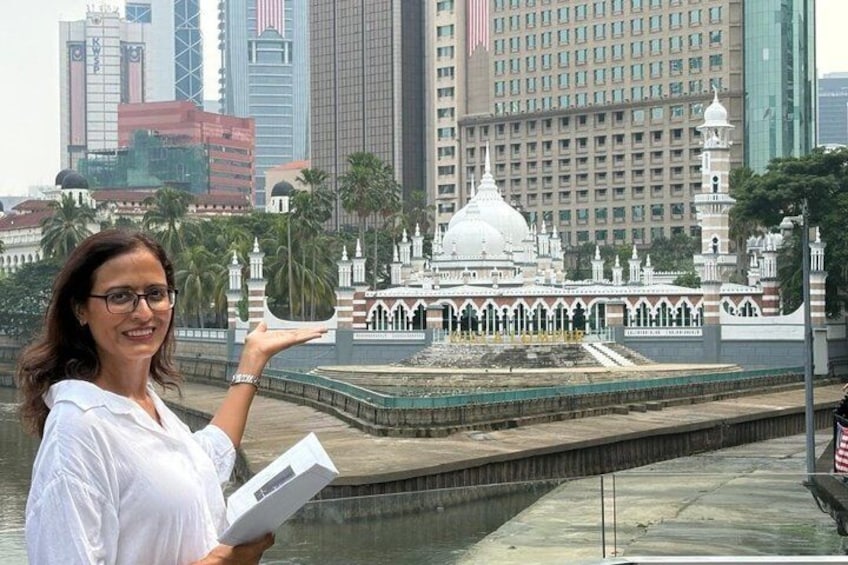 A woman holding a book, standing near a water feature with a white dome structure in the background. 1