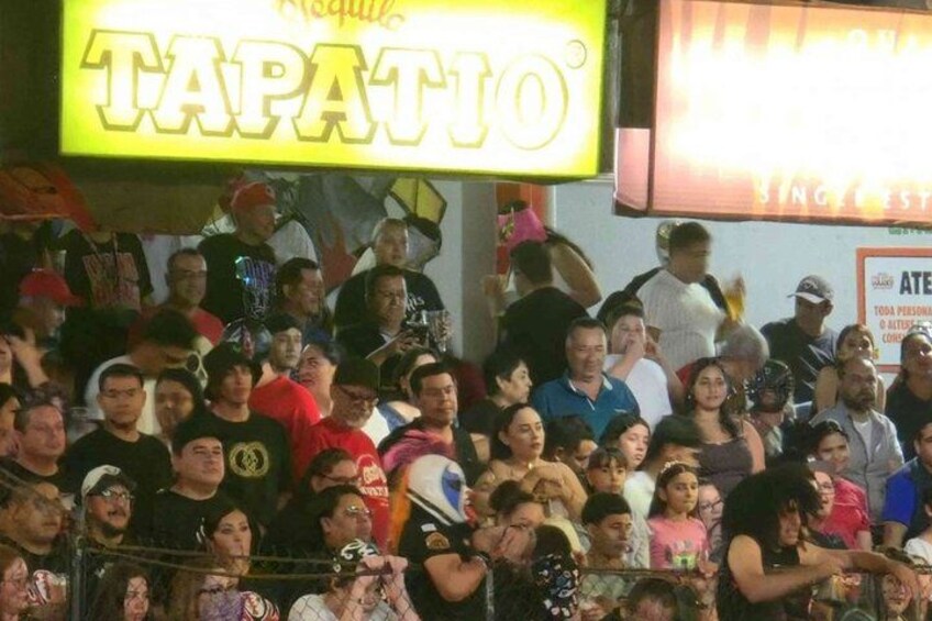 A crowded outdoor event with a neon sign reading 'TAPATIO'. 4