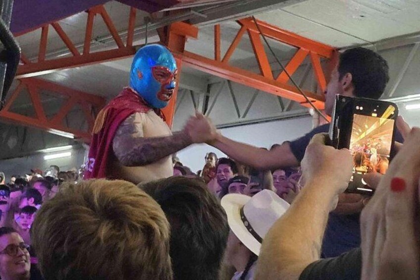 A person in a blue helmet and red cape interacting with a crowd, with a metal structure overhead. 3