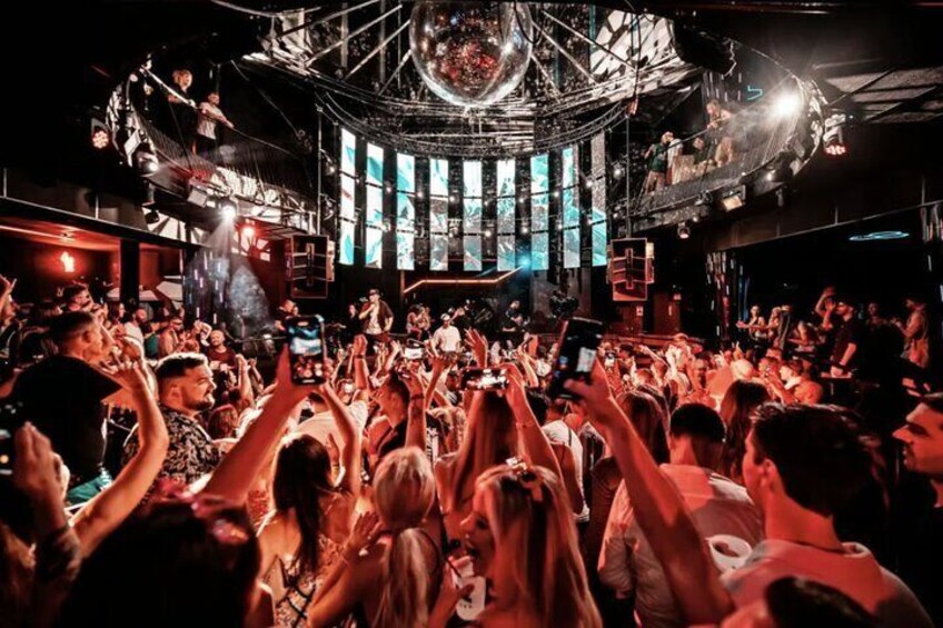 A crowded nightclub with a DJ booth and a disco ball. 2