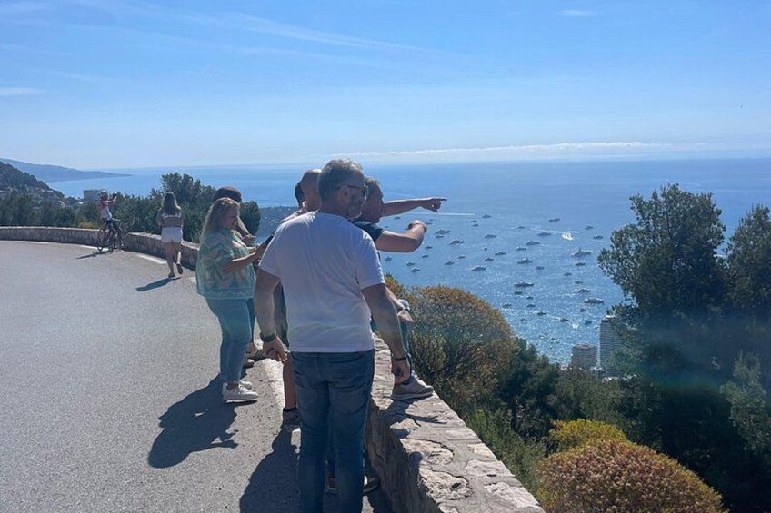 A coastal road with people enjoying the view, a cyclist, and boats in the distance. 2