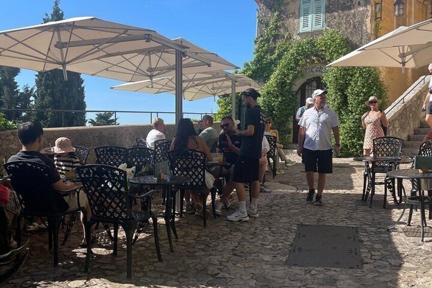 A cobblestone patio with outdoor seating, umbrellas, and people socializing. 4