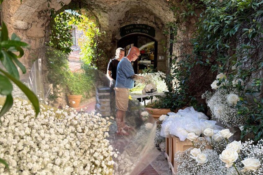 An outdoor market with flowers and plants, a stone archway, and a person browsing. 2