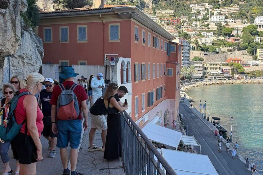 A coastal town with people walking along a cliffside path, overlooking a body of water. 3