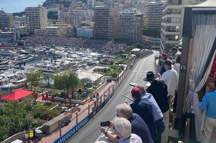 A crowded marina with boats, a crowd of people on a viewing platform, and a cityscape in the background. 3