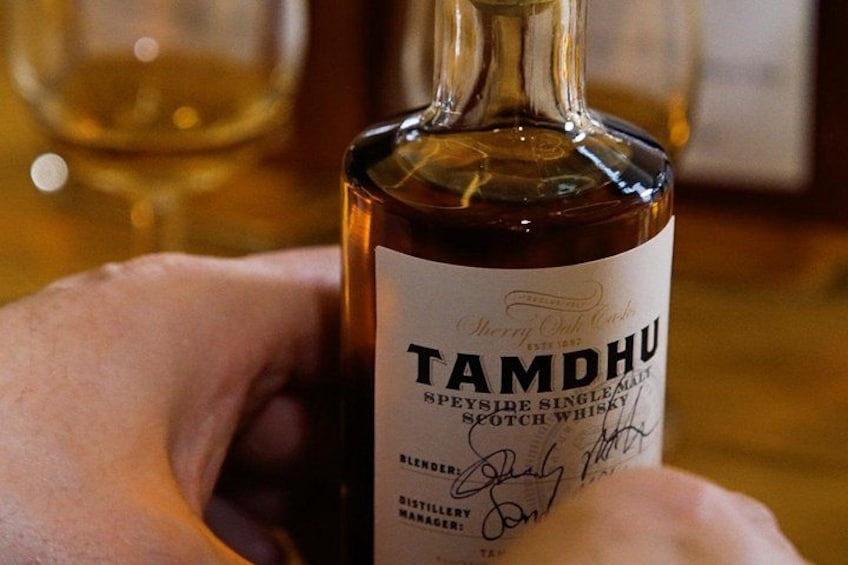 A bottle of Tamdhui whisky with a label, held by a person. 1