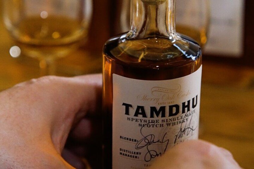 A bottle of Tamdhui whisky with a label, held by a person. 1