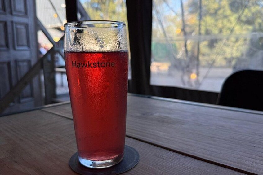 A glass of red beverage labeled 'Hawstone' on a wooden table by a window. 2
