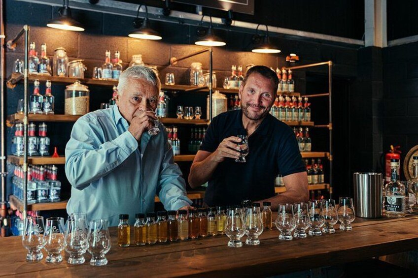 Two individuals at a bar with shelves of bottles and glasses in the background. 1