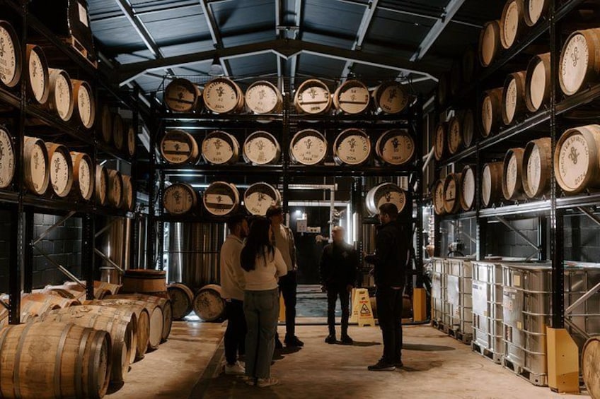 A warehouse with shelves of wooden barrels and a group of people standing in the center. 2