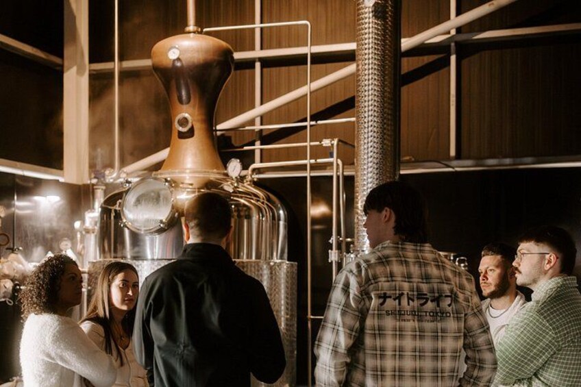 A group of people observing a large copper distillation apparatus in an industrial setting. 3