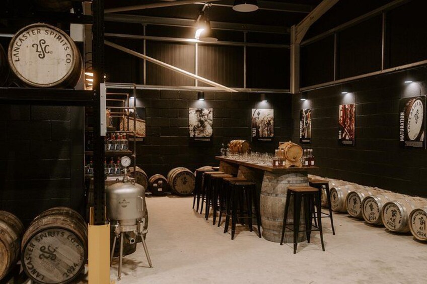 A bar area with wooden stools, a bar counter, and a large beer keg. There are barrels and a large clock on the wall. 4