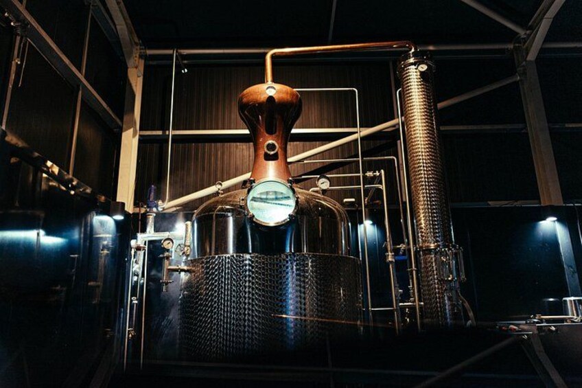 A distillery setup with copper equipment, a large tank, and a mesh-covered vessel. 2