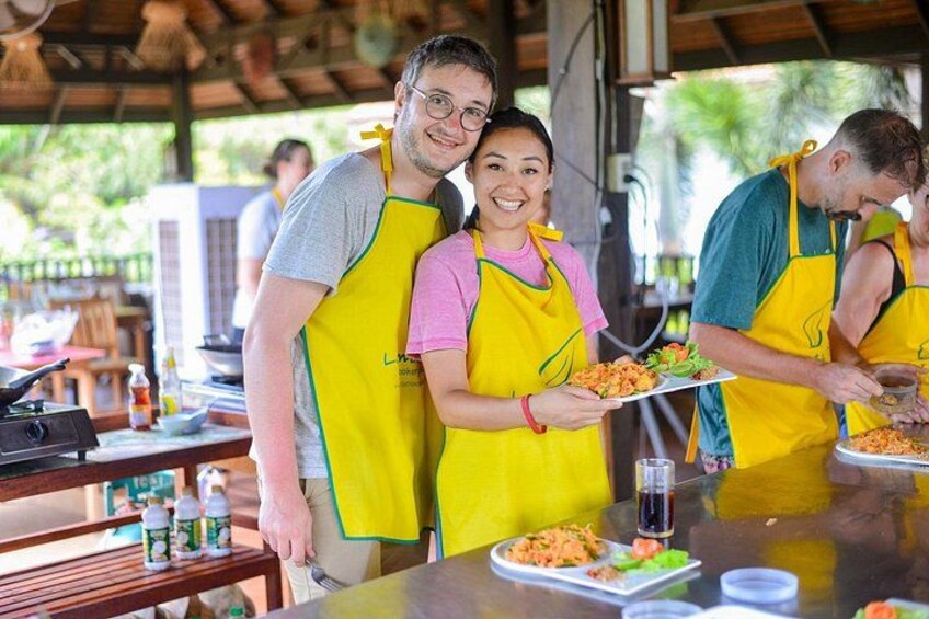 Persone con grembiuli gialli preparano cibo in un'area cottura all'aperto, con tavoli e attrezzature. 4
