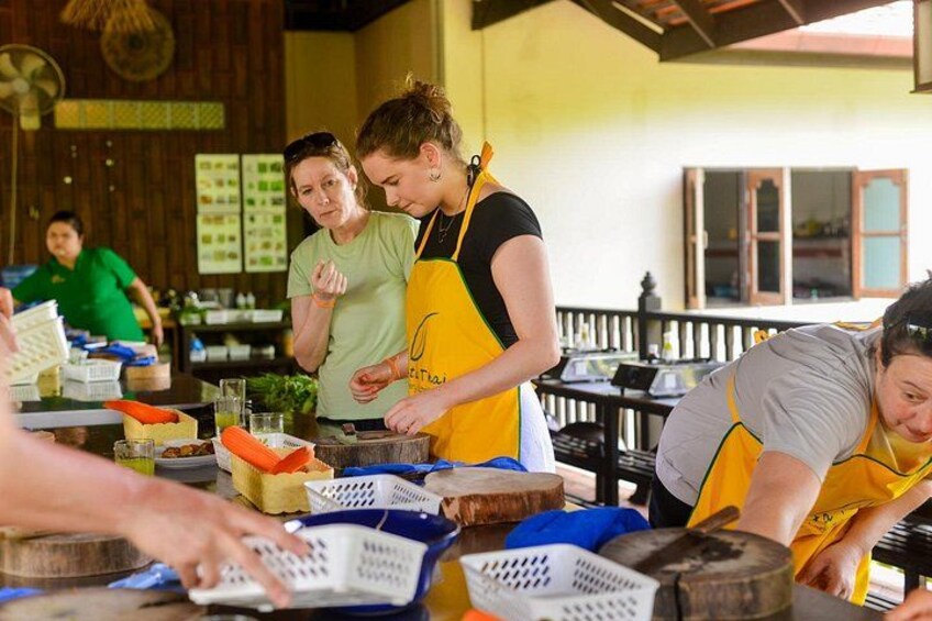 People wearing aprons, working with food items on a table in a kitchen setting. 3