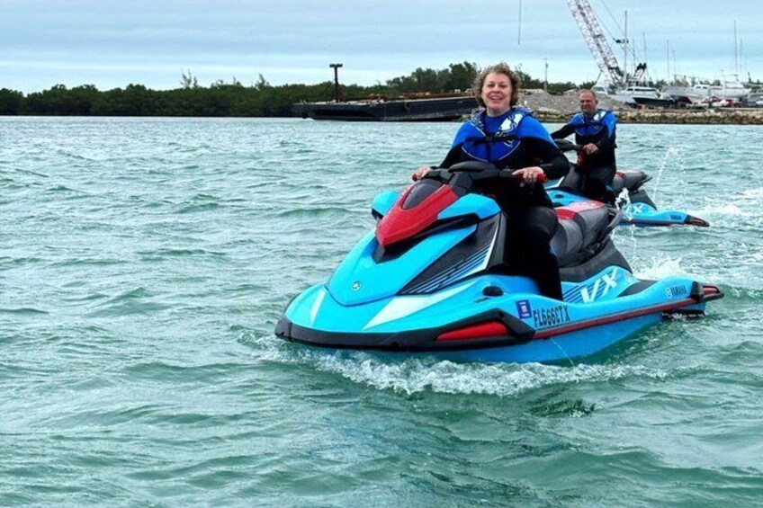 Two people on a jet ski on a body of water with a crane and boats in the background. 3