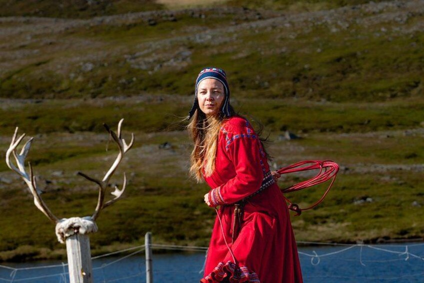 Una persona con un vestido rojo sosteniendo un lazo, de pie cerca de una masa de agua con una colina cubierta de hierba al fondo. 2