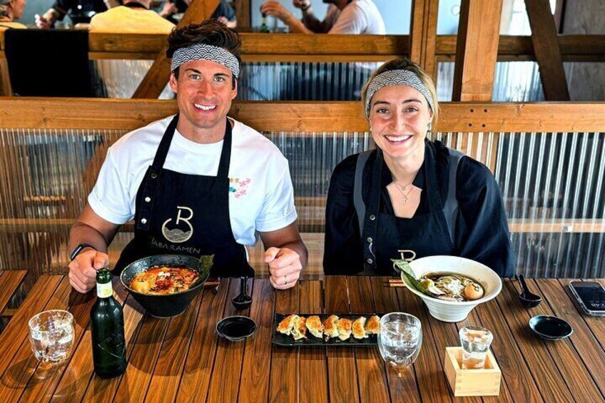 Two people sitting at a wooden table with bowls of food and a bottle of water. 1