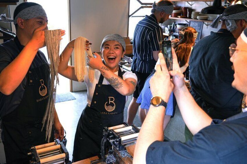People in a kitchen, some wearing aprons with a logo, preparing food. 3