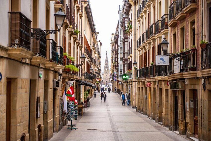 Una calle estrecha flanqueada por edificios históricos, algunos con balcones y plantas. 5