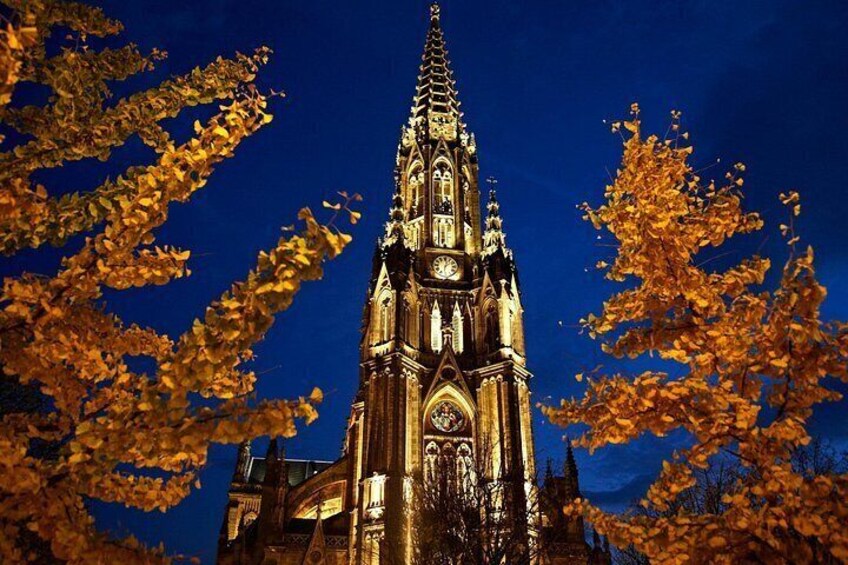 Una iglesia de estilo gótico con una aguja alta y un campanario, rodeada de árboles de tonos otoñales. 4