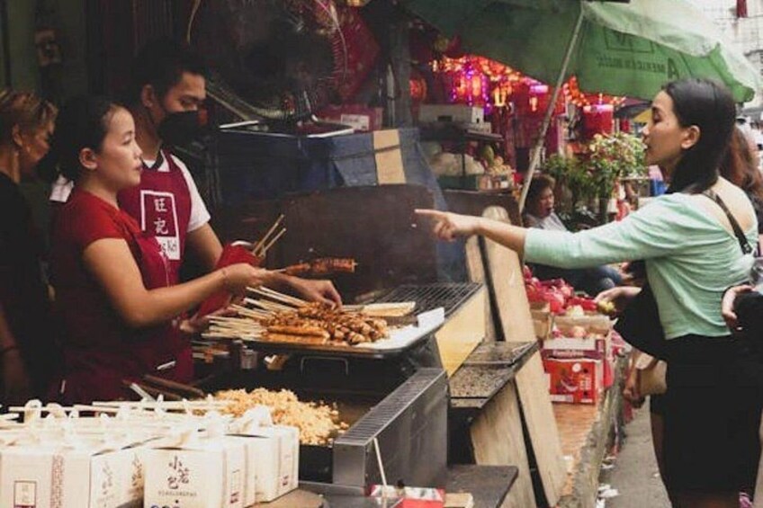 A street food vendor grilling skewers, with a customer pointing at the food. 4