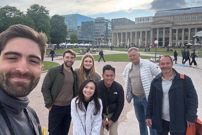 A group of people standing in a public square with buildings and trees in the background. 3
