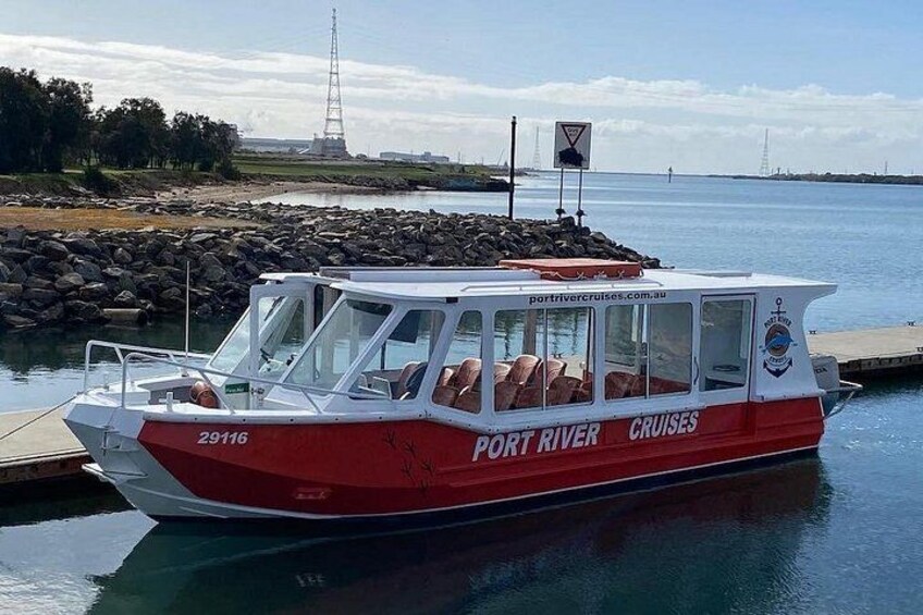 Een rode en witte boot met de naam 'Port River Cruises' afgemeerd aan een steiger. 2