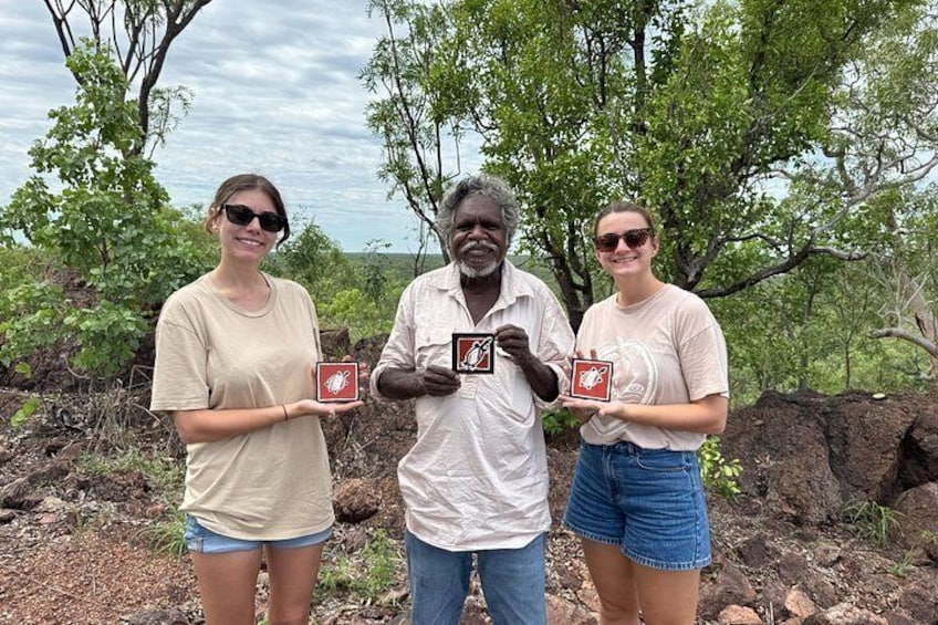 Three people holding framed pictures outdoors with trees and rocky terrain in the background. 5