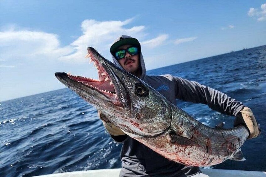 A person holding a large fish with an open mouth, wearing a hat and gloves, on a boat in the ocean. 2